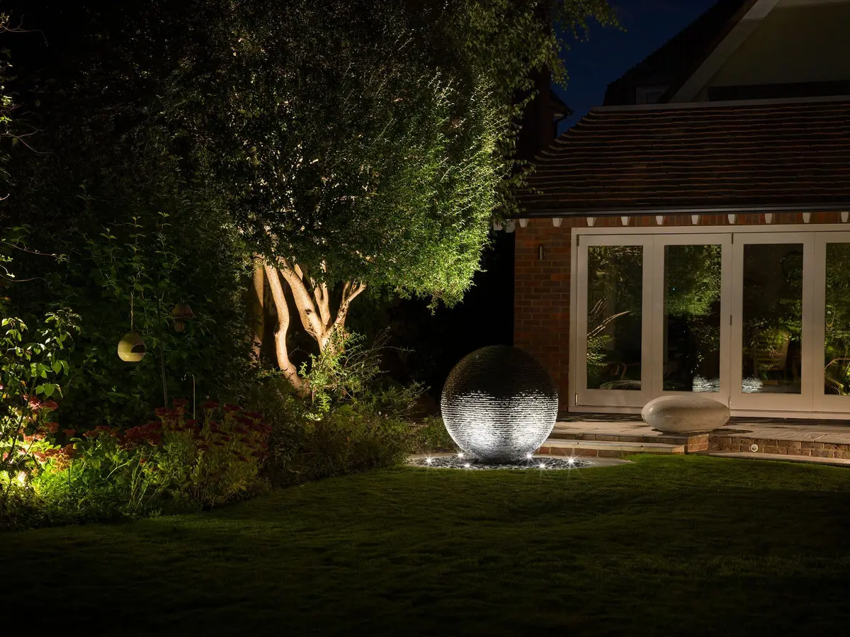 Illuminated slate sphere water feature glowing beside a lit patio and bifold doors on an Eastbourne home at dusk